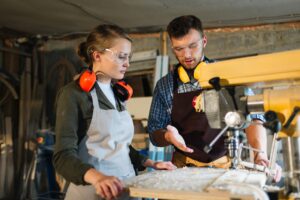 Male mentor explaining machine operation to a female student in a trade school workshop during vocational training