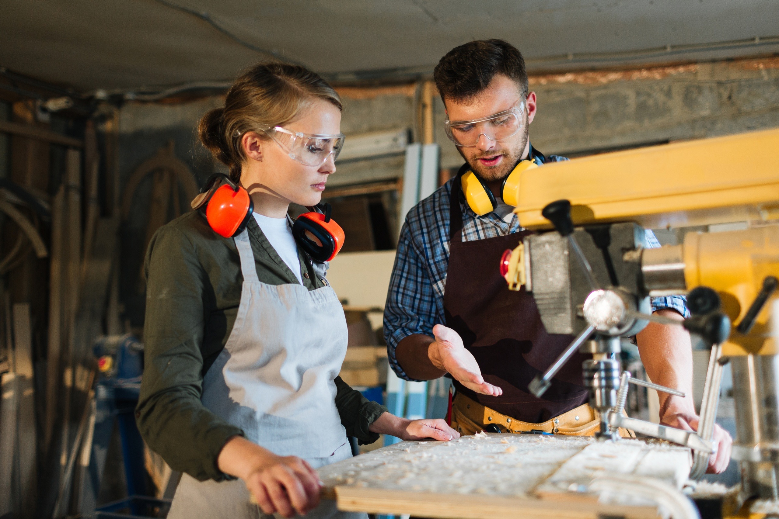 Male mentor explaining machine operation to a female student in a trade school workshop during vocational training