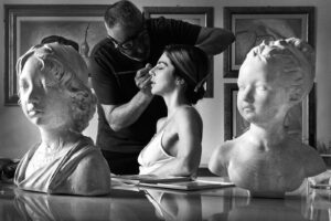 Black and white documentary photograph of a bride getting her makeup done framed by classical sculptures